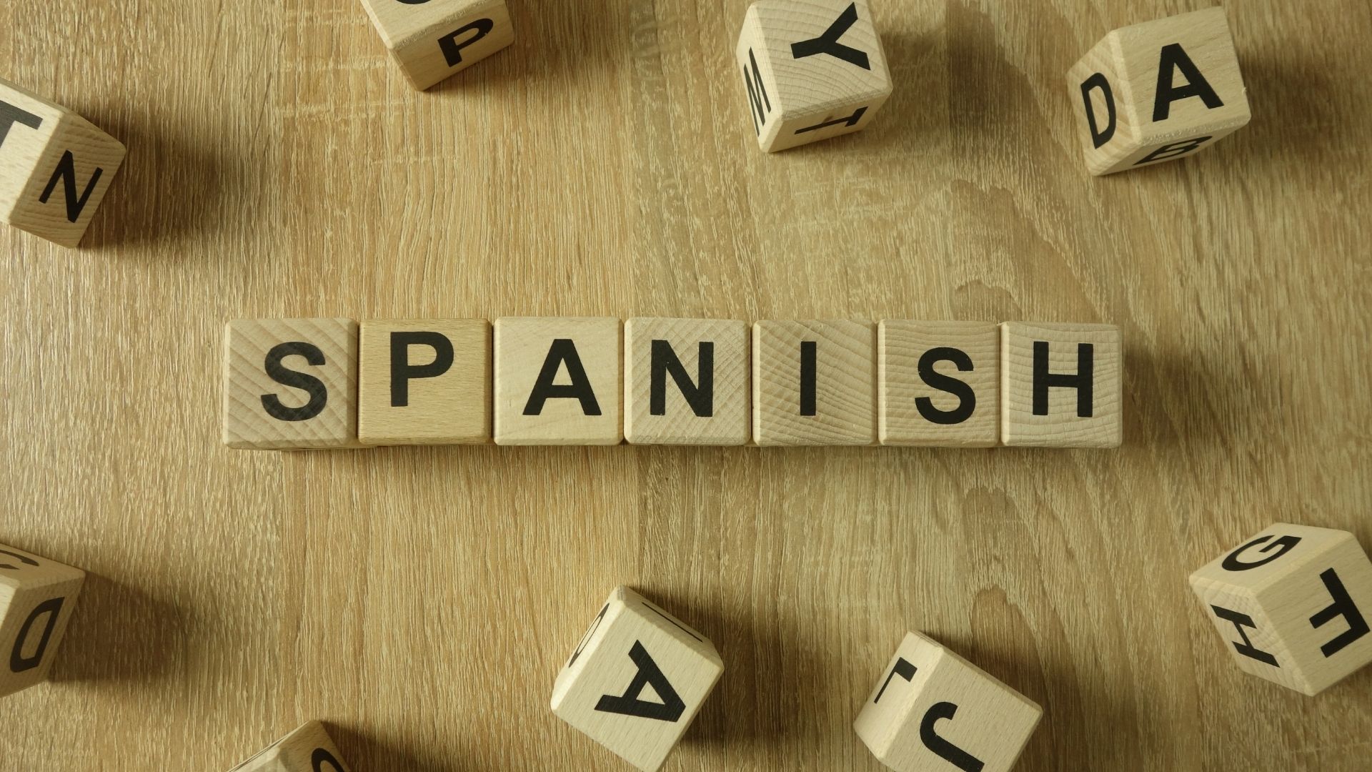 Wooden alphabet blocks spelling SPANISH on a wooden table, representing multilingual sermon translation